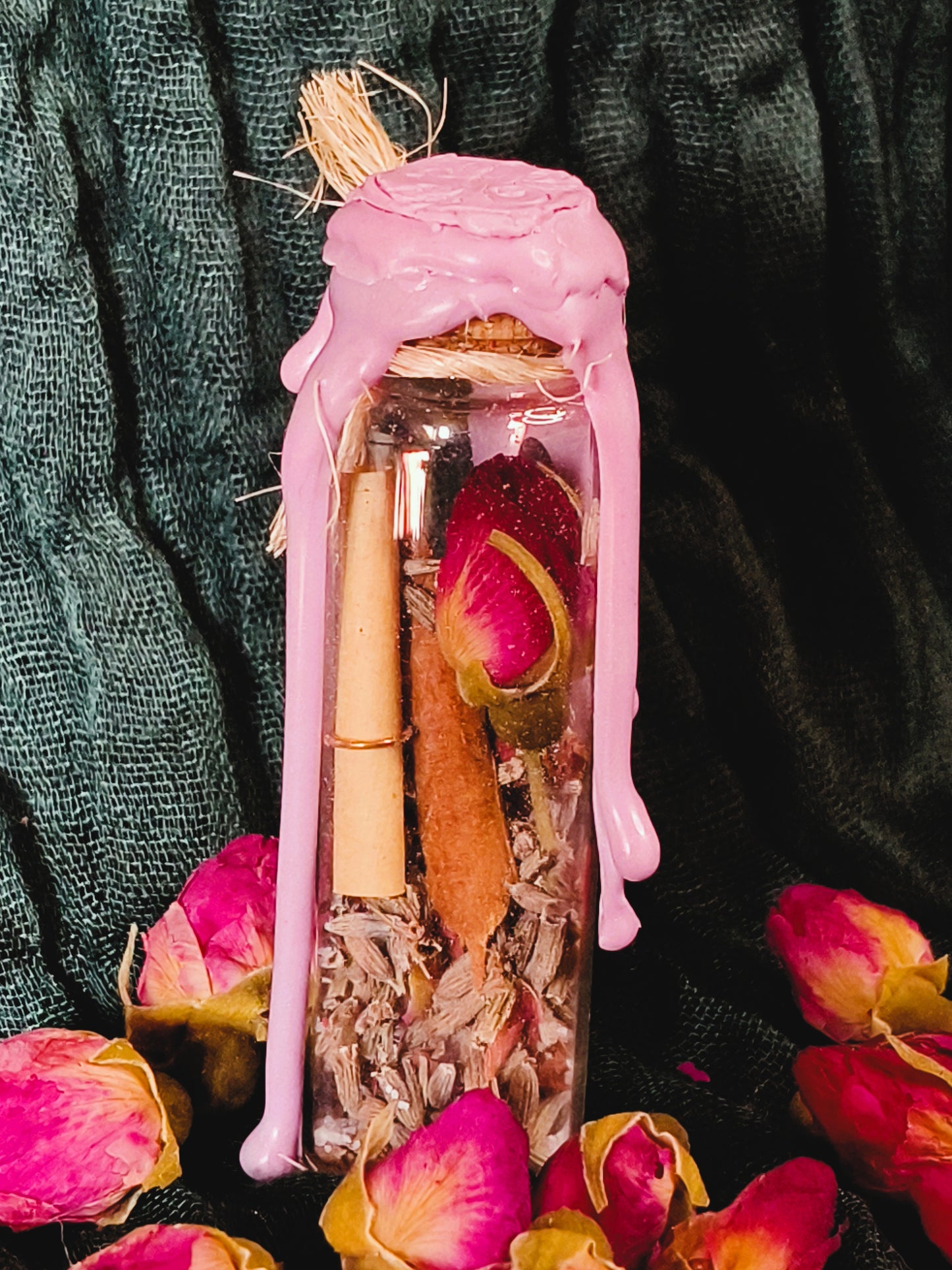 Close up of a love spell jar with pink dripping wax and natural raffia tie, containing dried roses, lavender, pink quartz and a rolled parchment, handmade by Malika's Realm