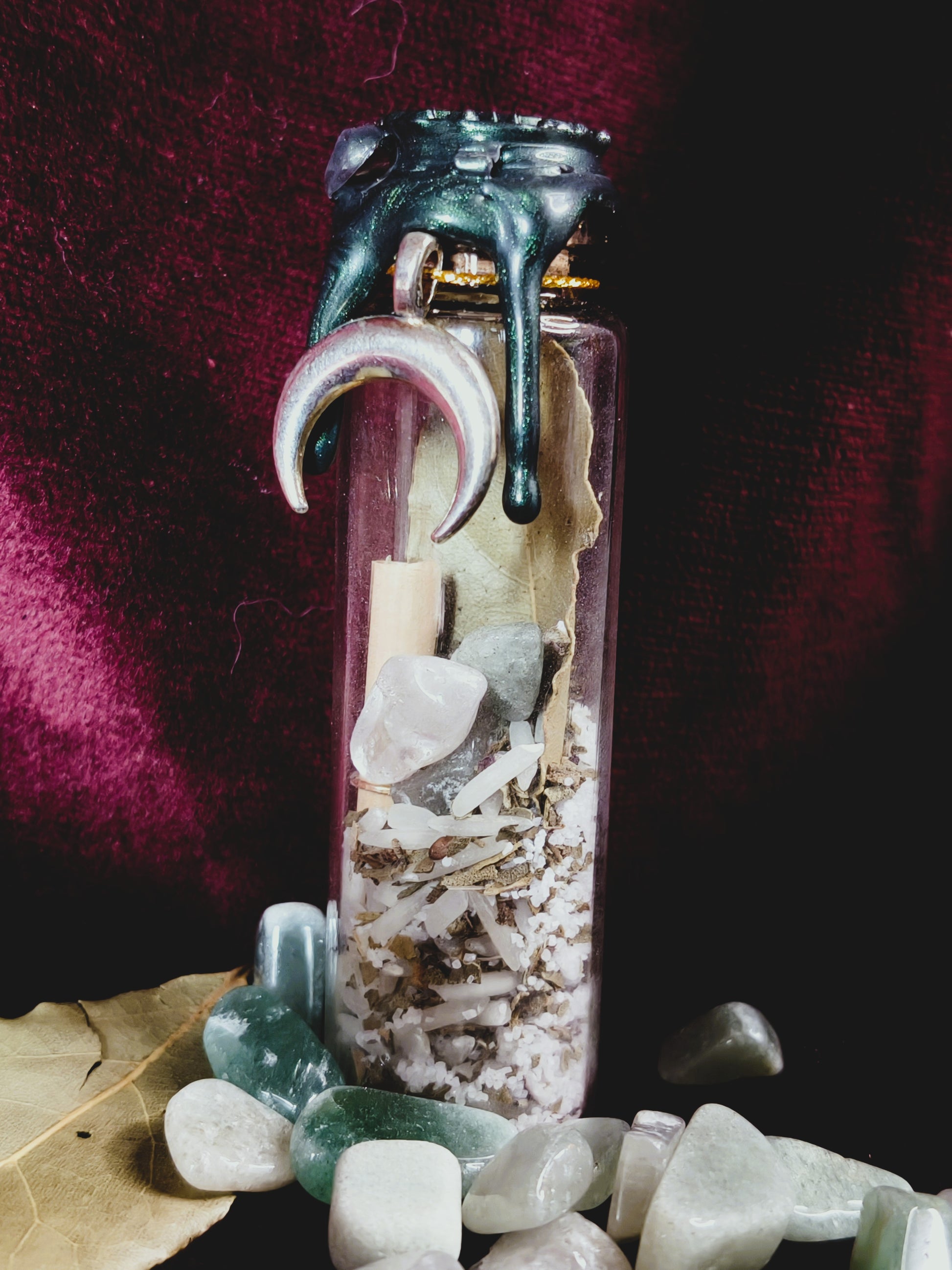 Close up of a good luck spell jar with black and green dripping wax, containing herbs, salt, rice, crystals and a charm pendant, handcrafted intention bottle by Malika's Realm